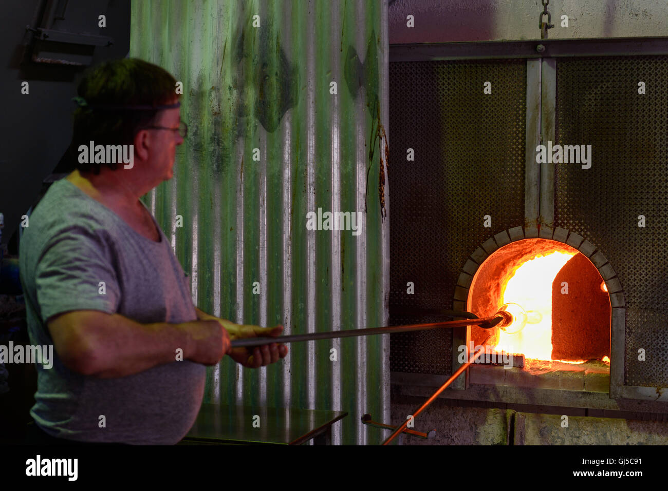 A glass blower working on Murano, Venice, Italy, heating the glass on a pole in a furnace Stock Photo