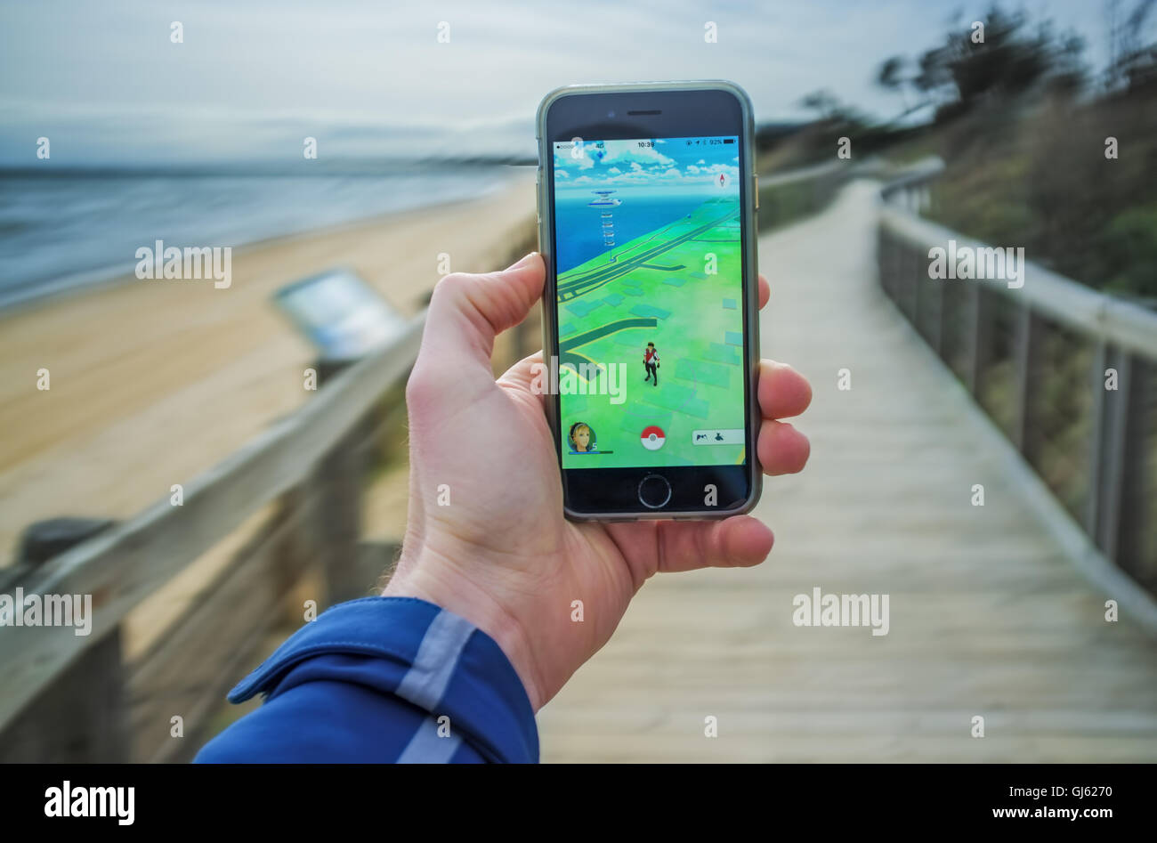 Melbourne, Australia - August 12, 2016: Male hand holding iPhone 6 with Pokemon Go game on boardwalk near ocean shore. Stock Photo