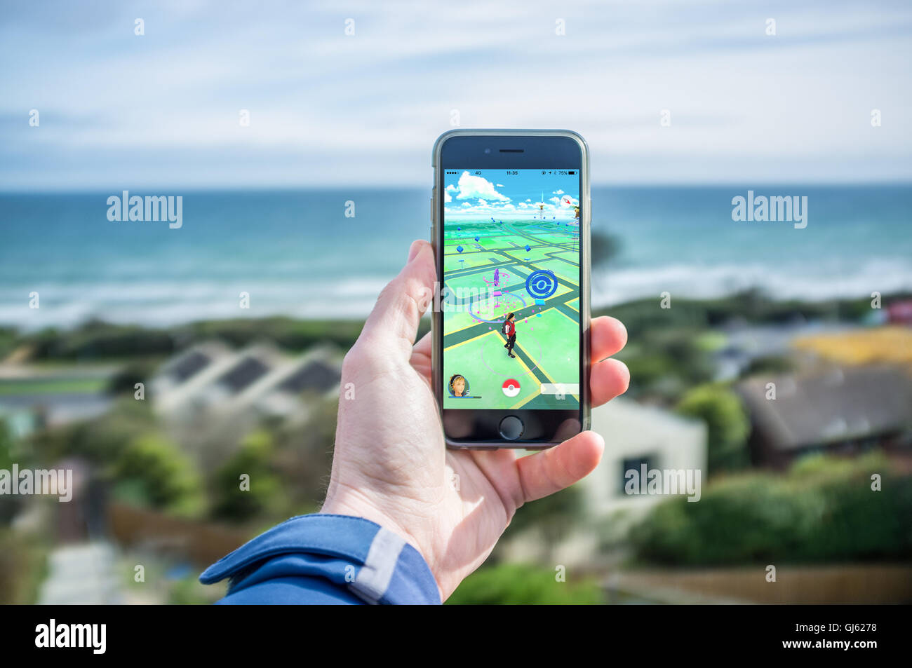 Melbourne, Australia - August 12, 2016: Male hand holding iPhone 6 with Pokemon Go game in residential area facing ocean Stock Photo