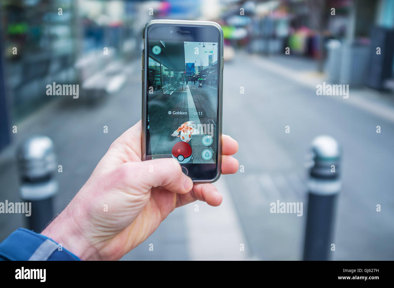 Melbourne, Australia - August 12, 2016: Male hand holding iPhone 6 with Pokemon Go game  catching Goldeen on a busy street Stock Photo