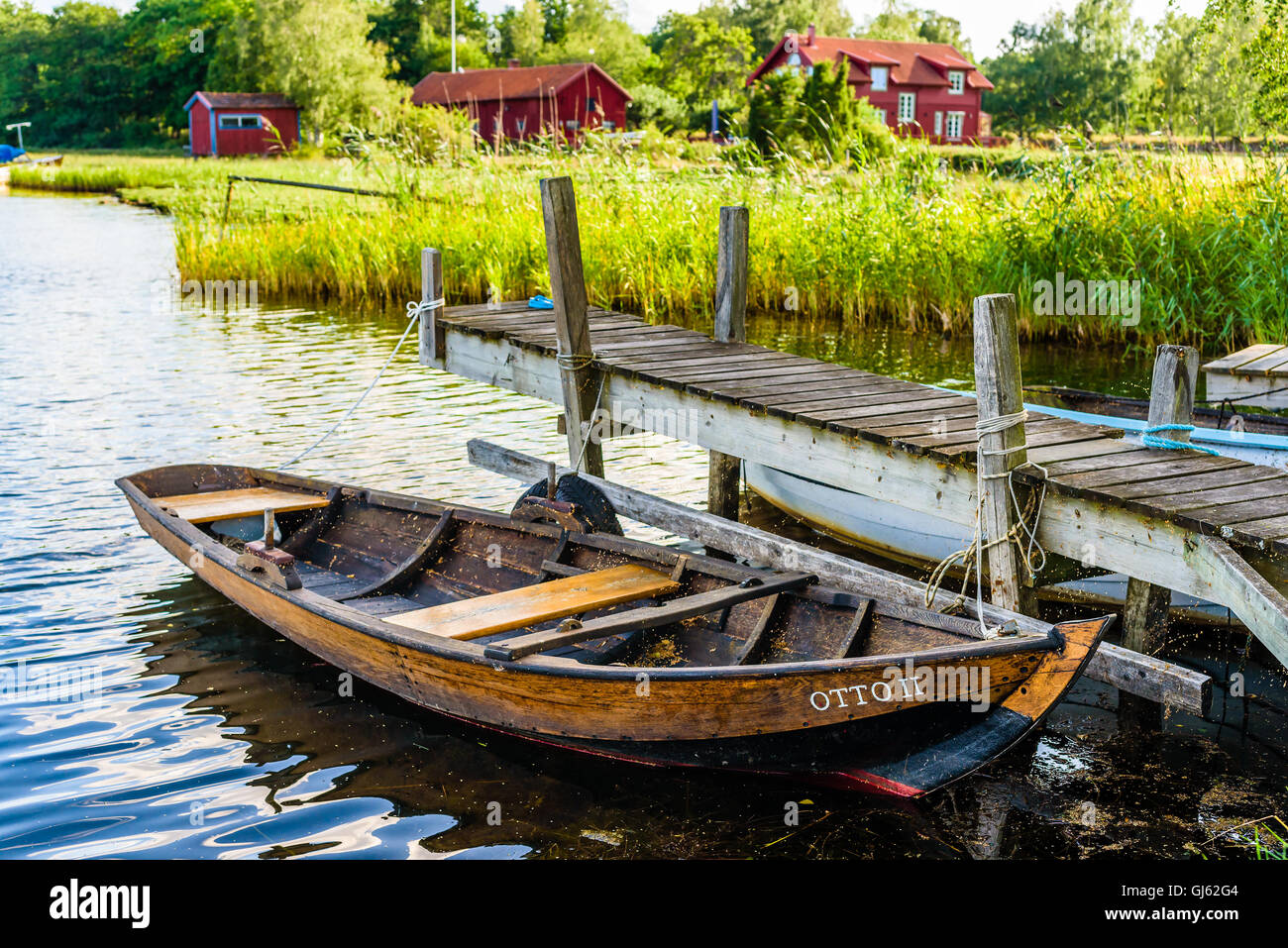 Pataholm, Sweden - August 9, 2016: Traditional wooden skiff named Otto II moored at small pier with red homestead in the backgro Stock Photo
