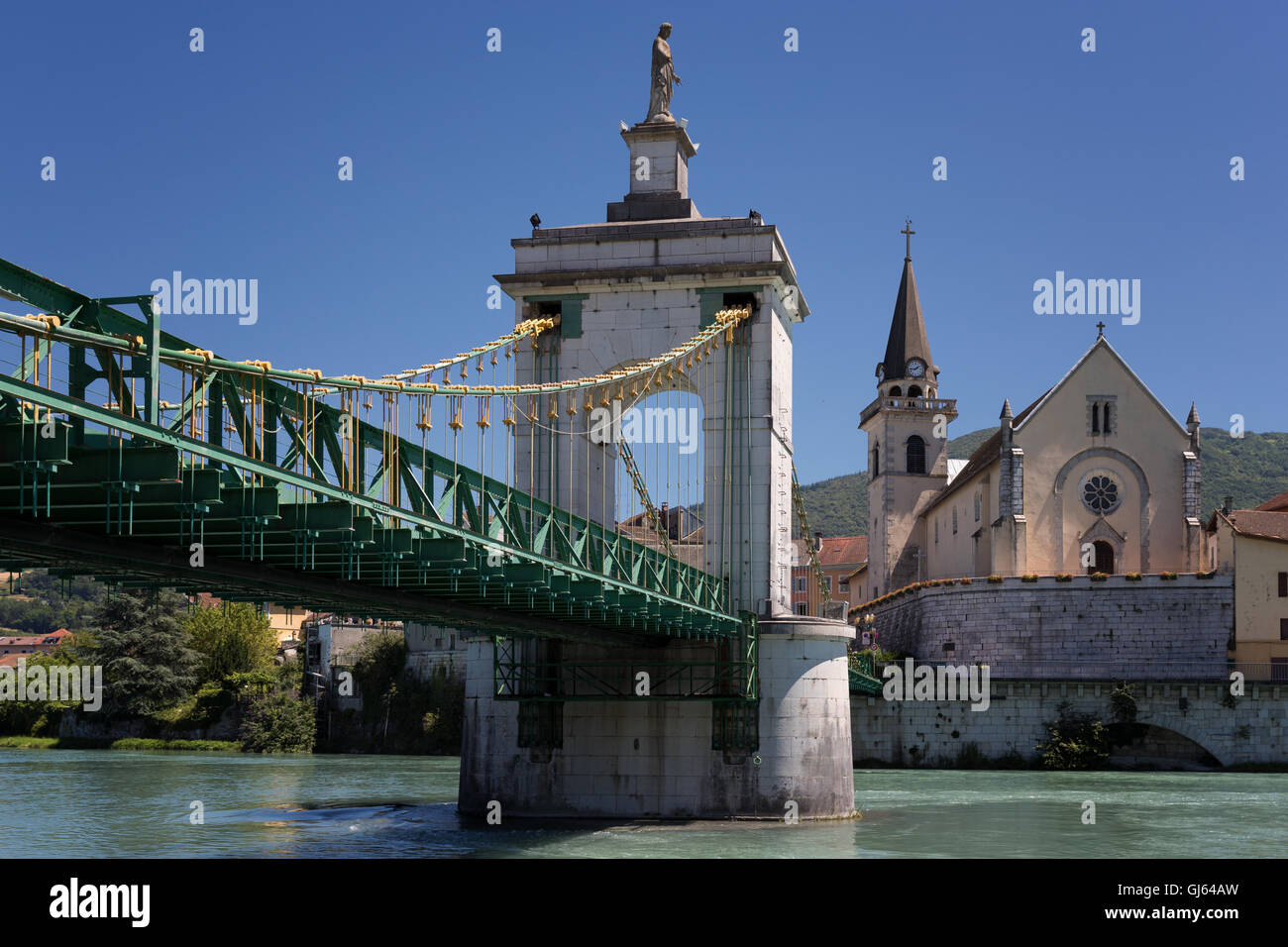 Suspended bridge above the river with church in the background under blue sky Stock Photo
