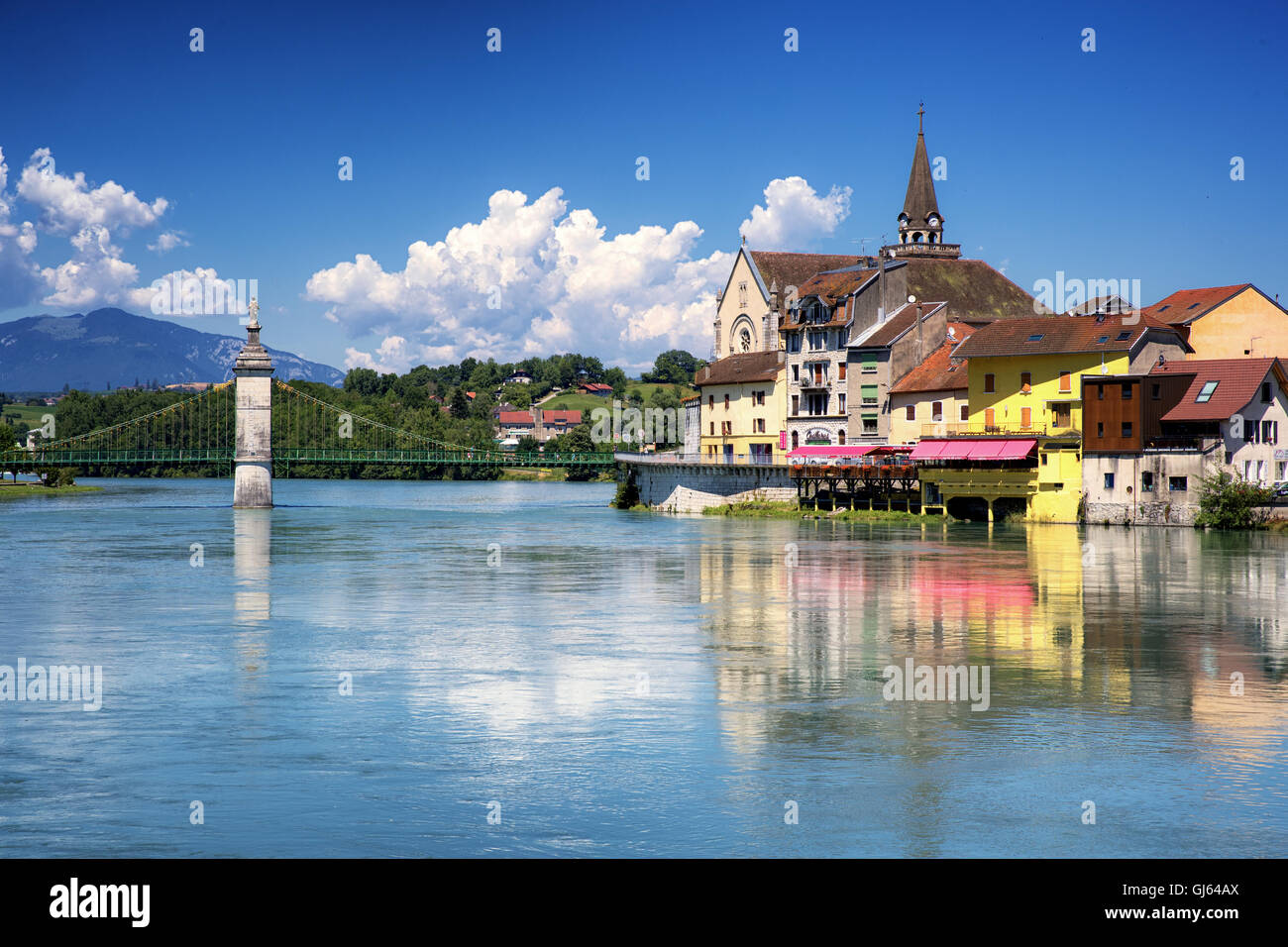 Suspended bridge above the river with a village and a church under blue sky Stock Photo