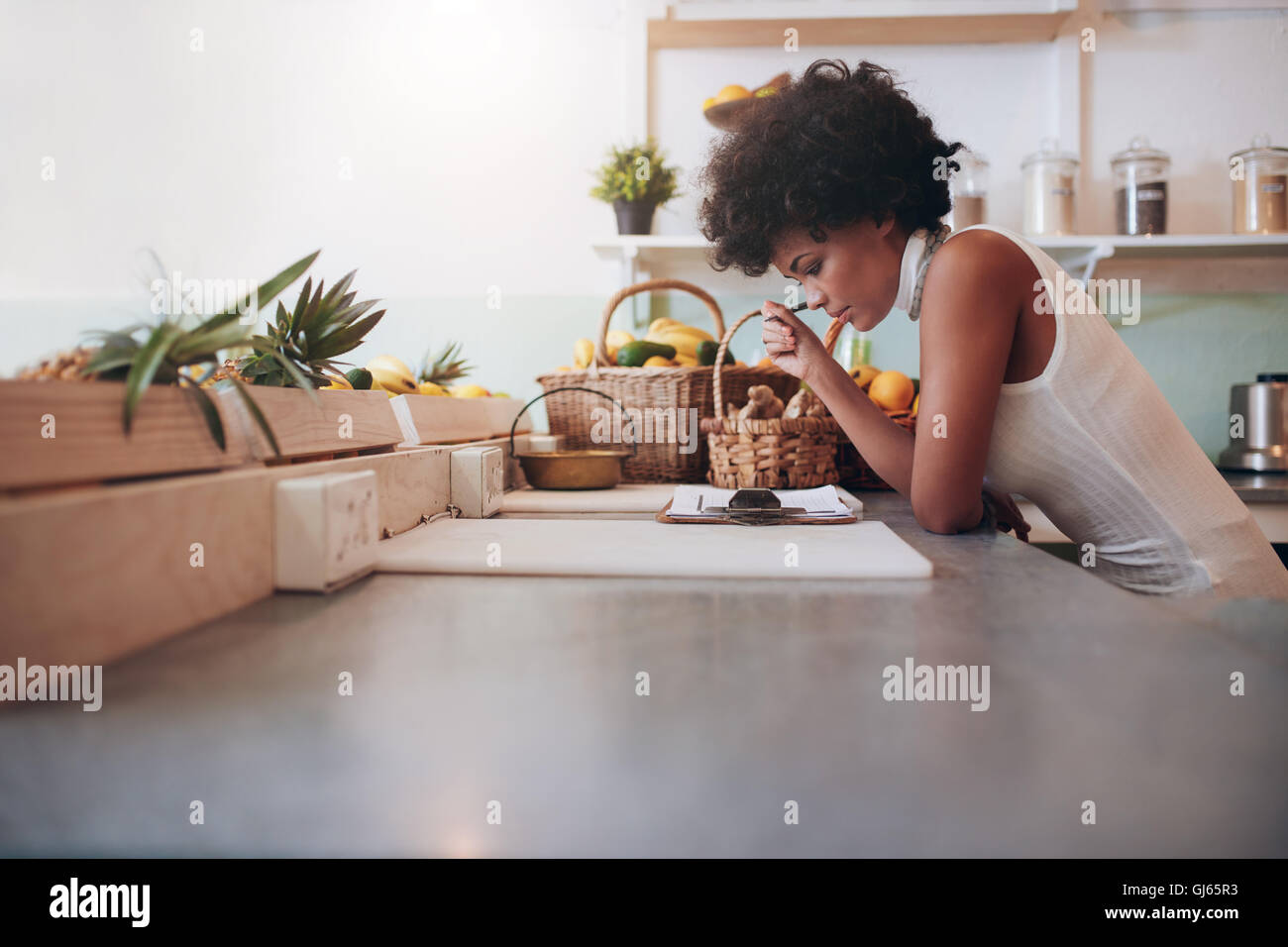 Female proprietor of a juice bar calculating a her business expenses. African young woman looking at the clip board on counter. Stock Photo