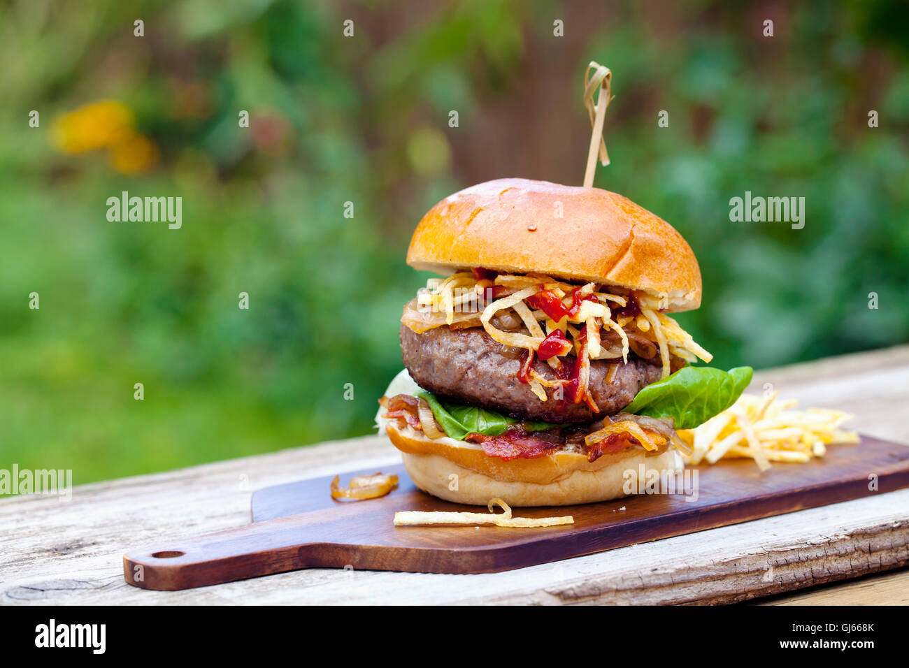 Beefburger with fried onions, bacon and string fries in brioche bun Stock Photo