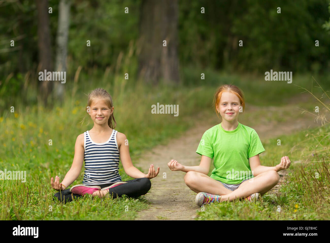 Two little cute girls sitting in the Lotus position in the Park. Yoga and a healthy lifestyle. Stock Photo