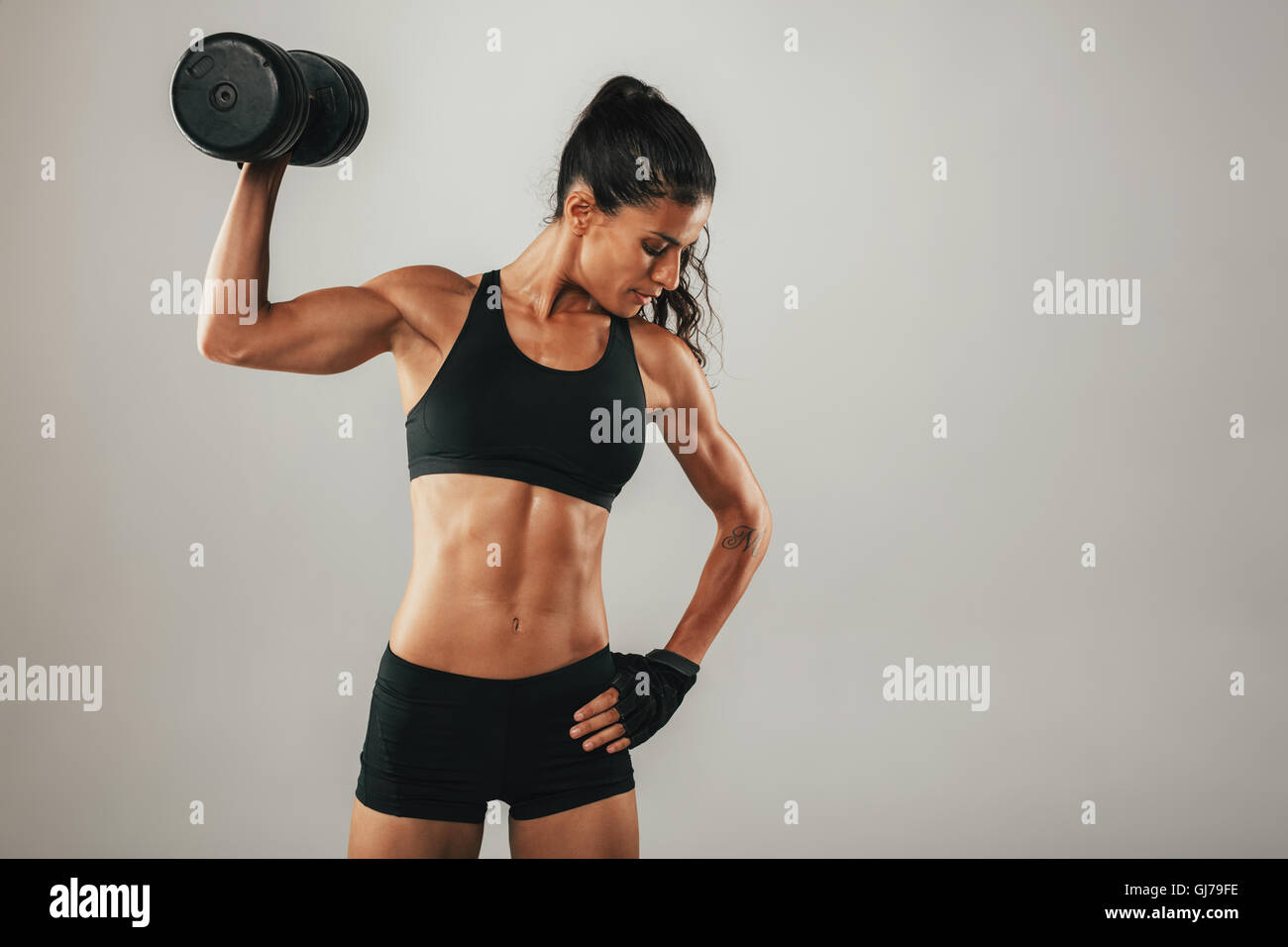 Toned muscular young woman working out with weights raising a