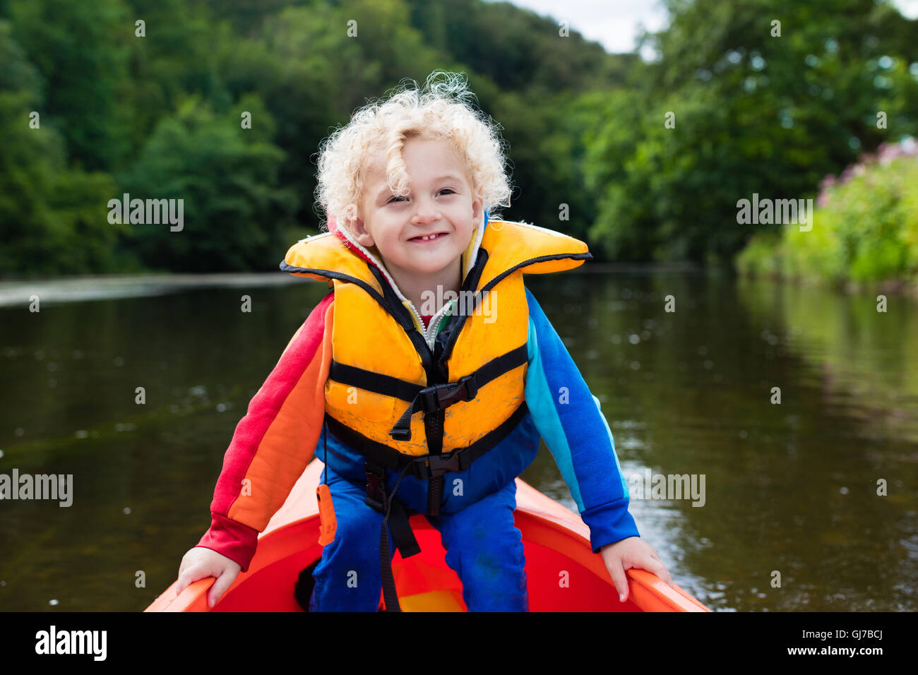 Happy kid enjoying kayak ride on beautiful river. Little curly toddler ...