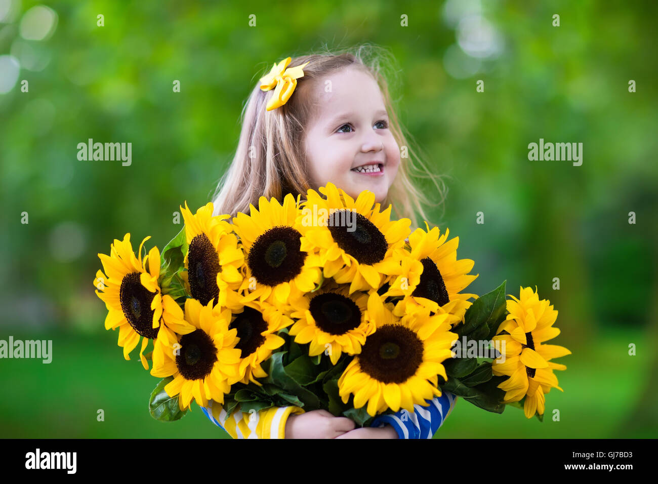 Happy laughing little girl holding sunflower bouquet. Child playing
