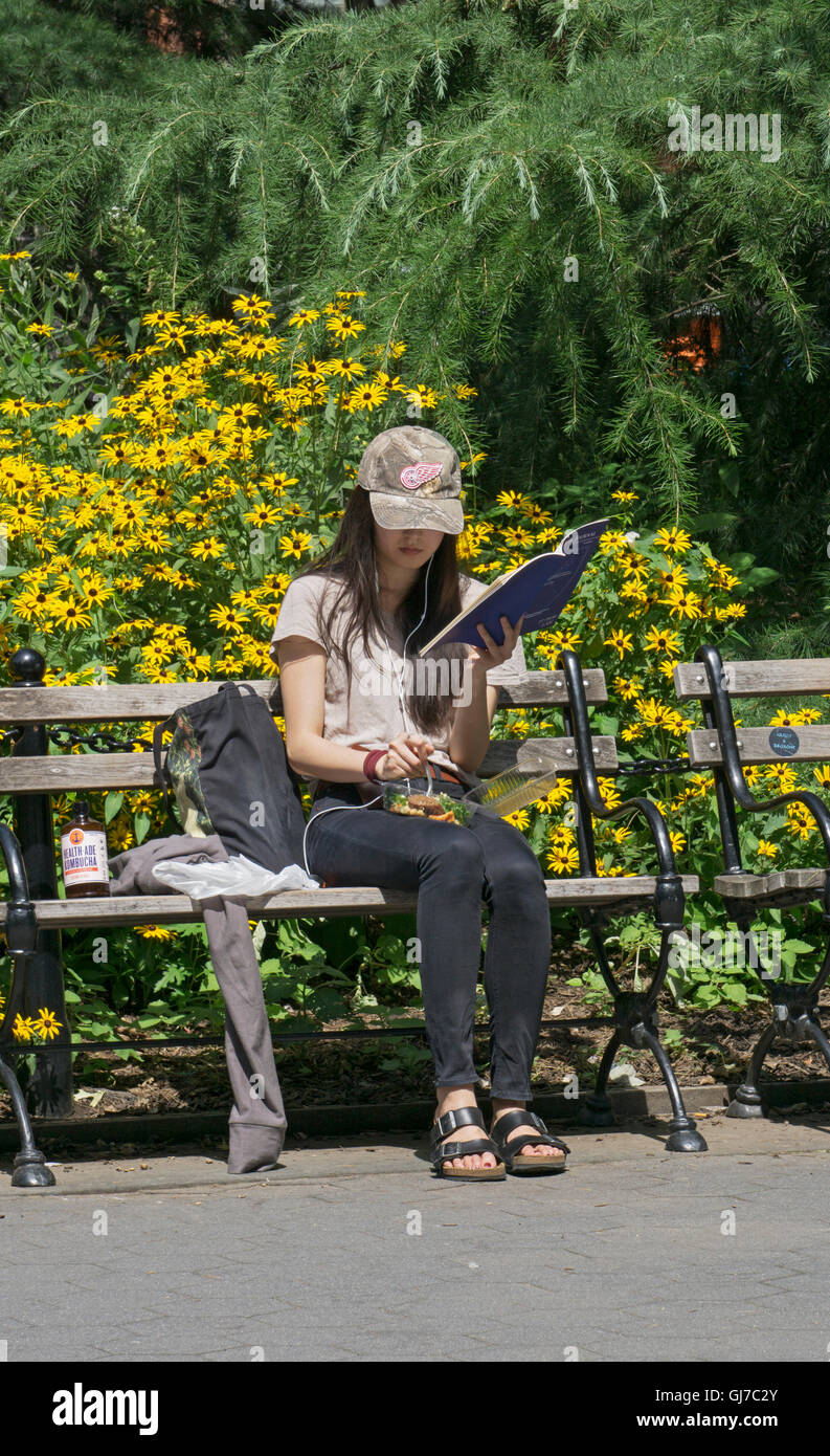 An woman multi tasking in Washington Square Parke in Manhattan - reading, eating & listening to music Stock Photo