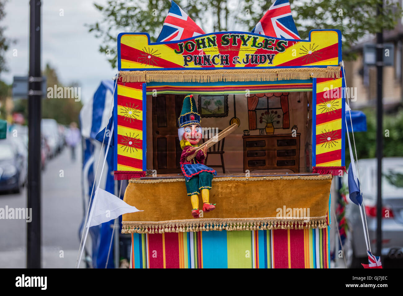 A full body Mr Punch sits at his Punch and Judy glove puppet booth holding a stick Stock Photo