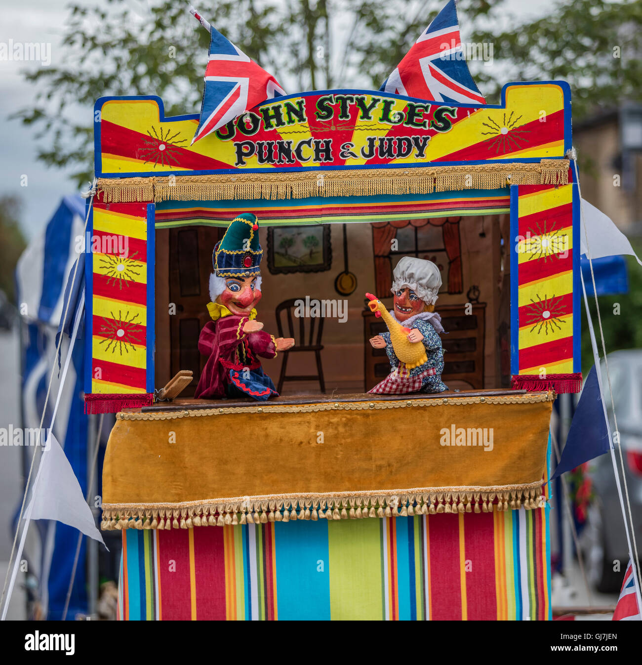 Mr Punch with Judy holding a chicken in a Punch and Judy puppet booth