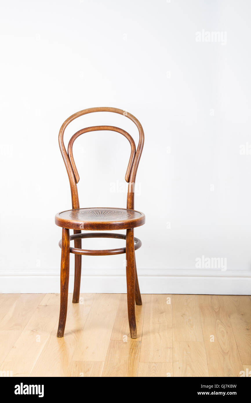 A single antique wooden chair, on a polished pine floor against a white wall Stock Photo