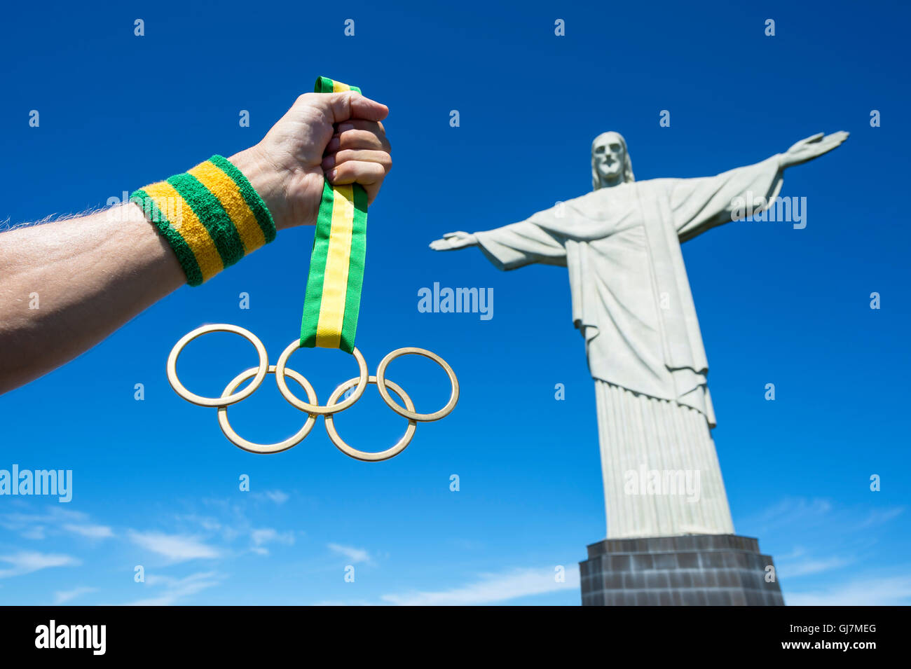 RIO DE JANEIRO - MARCH 21, 2016: Hand holding Olympic rings gold medal hanging from ribbon in clear blue sky next to Corcovado. Stock Photo