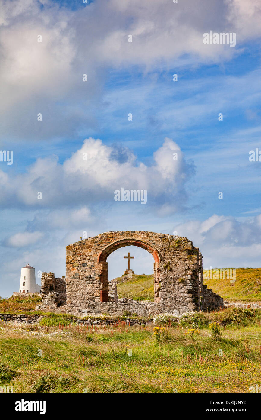The ruined Church of St Dwynwyn, looking through a window to a large  cross, and the old lighthouse, Twr Mawr, on the tidal... Stock Photo