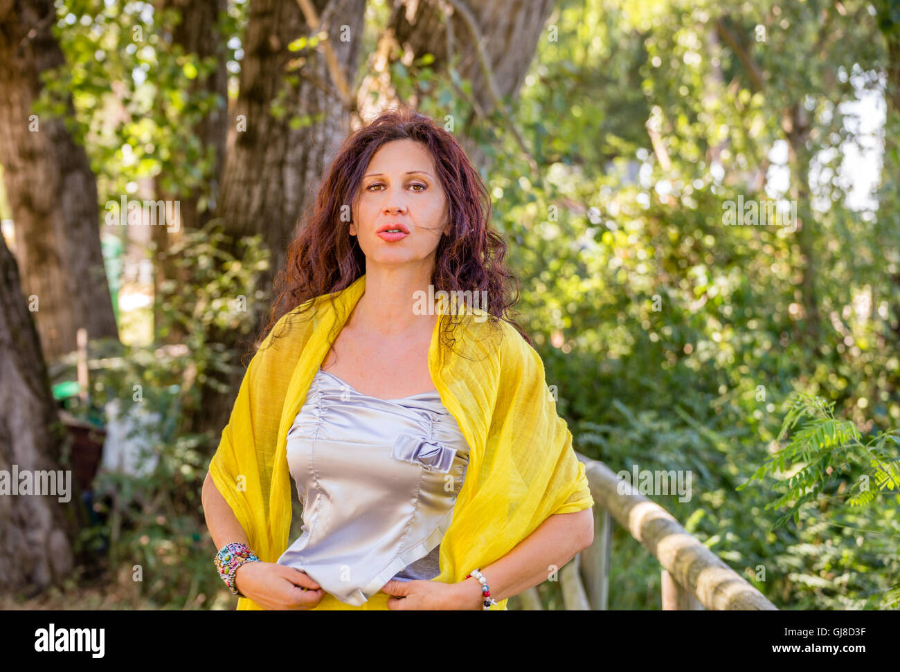 elegant and glamorous senior woman with yellow shawl and silver top is talking in a green park Stock Photo