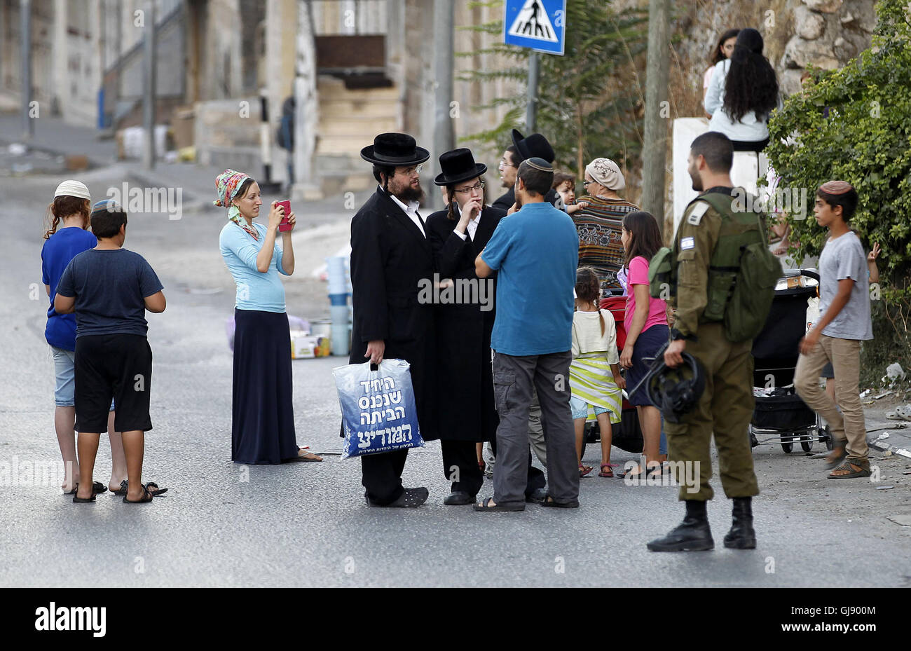 Hebron, West Bank, Palestinian Territory. 14th Aug, 2016. An Israeli soldier stands guard as Israeli settlers walk on a street in a Palestinian neighbourhood in the divided West Bank city of Hebron as they are heading to the Jewish shrine of Atnaeil Ben Kinaz on August 14, 2016. Orthodox Jews mark on August 14 2016 the annual Tisha B'Av (Ninth of Av) fasting and a memorial day, commemorating the destruction of ancient Jerusalem temples some 2000 years ago Credit:  Wisam Hashlamoun/APA Images/ZUMA Wire/Alamy Live News Stock Photo