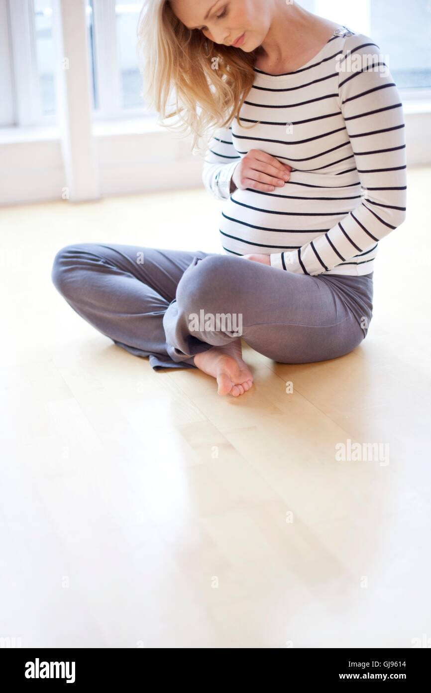 MODEL RELEASED. Pregnant woman sitting cross legged on the floor Stock