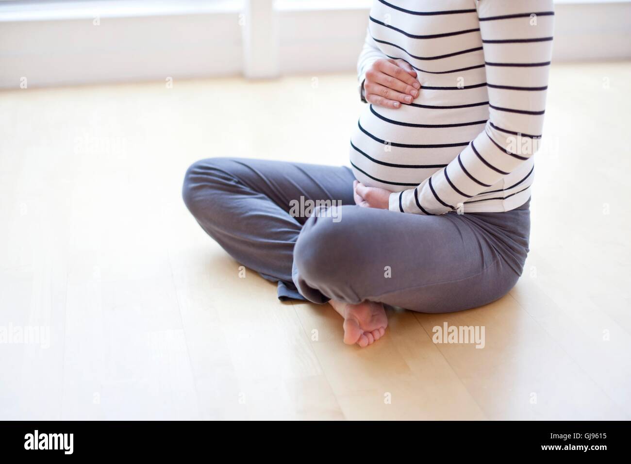 MODEL RELEASED. Pregnant woman sitting cross legged on the floor. Stock Photo