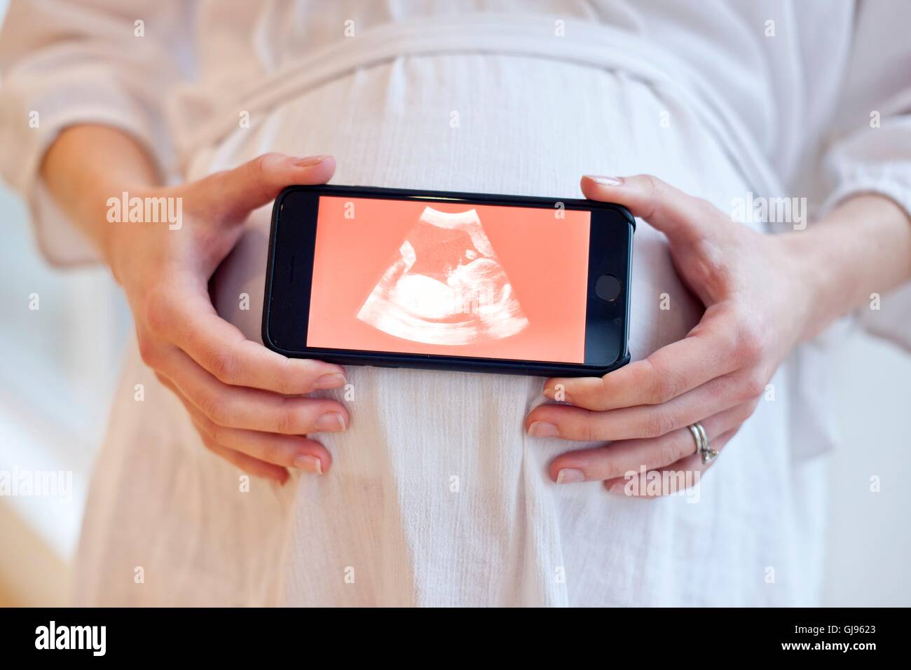 MODEL RELEASED. Pregnant woman holding smartphone with baby scan. Stock Photo