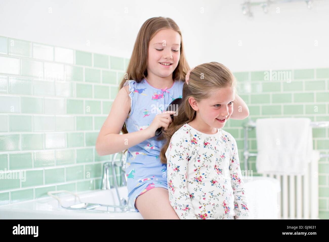 PROPERTY RELEASED. MODEL RELEASED. Big sister brushing little sister's hair in bathroom. Stock Photo