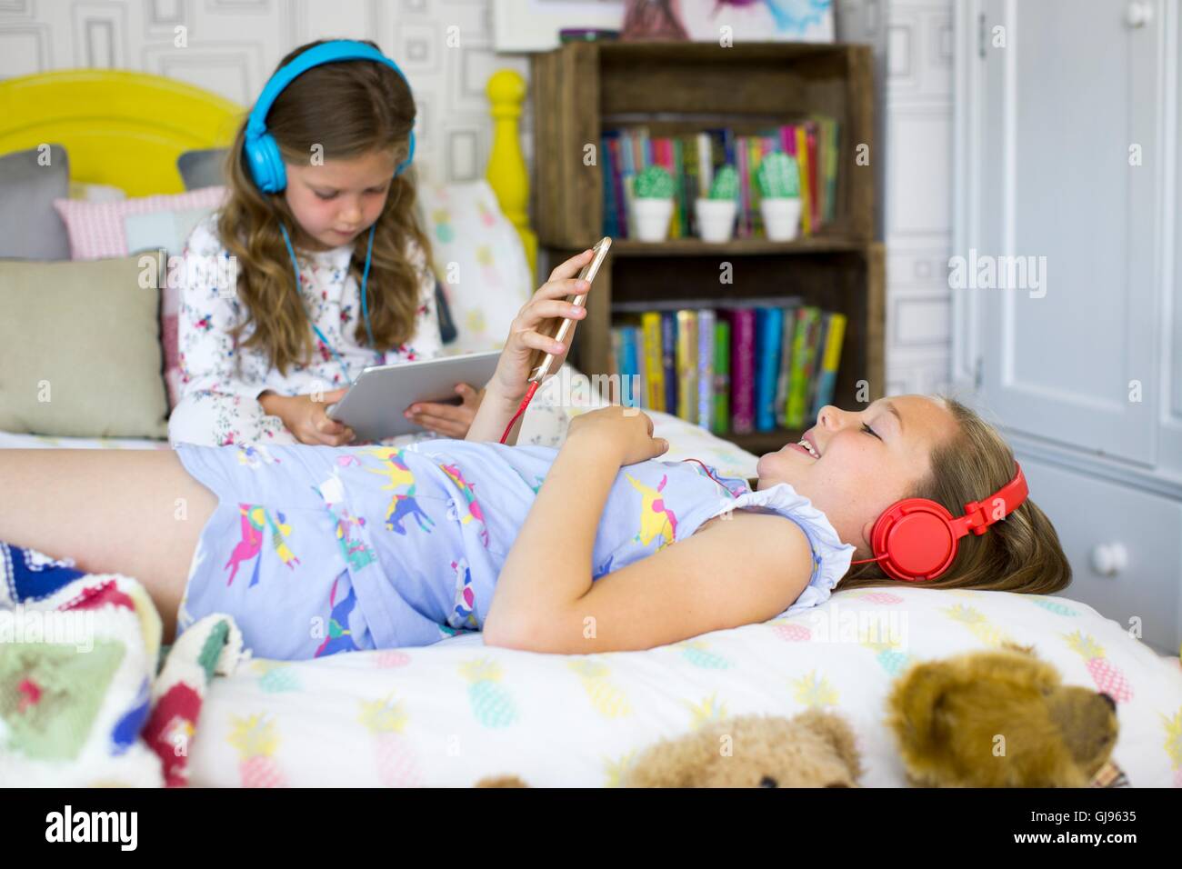 PROPERTY RELEASED. MODEL RELEASED. Two sisters in bedroom listening to music and watching movies. Stock Photo