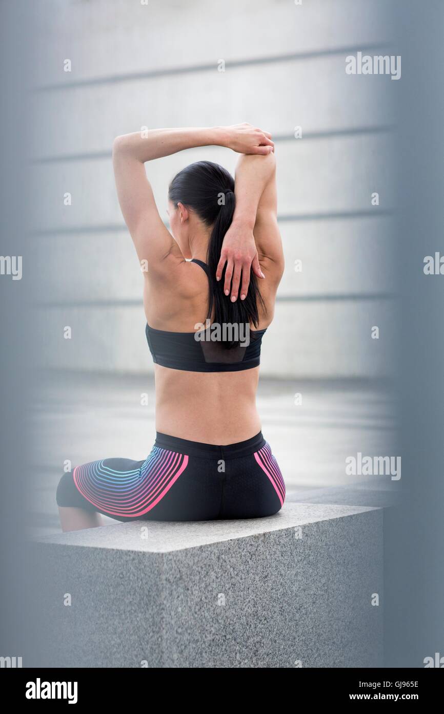 MODEL RELEASED. Young woman sitting on wall, stretching. Stock Photo