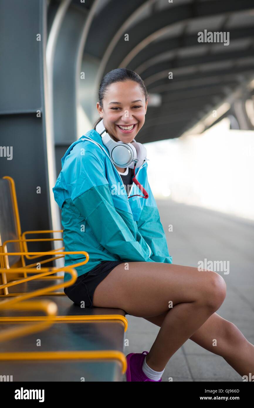 MODEL RELEASED. Young woman sitting on railway platform smiling. Stock Photo
