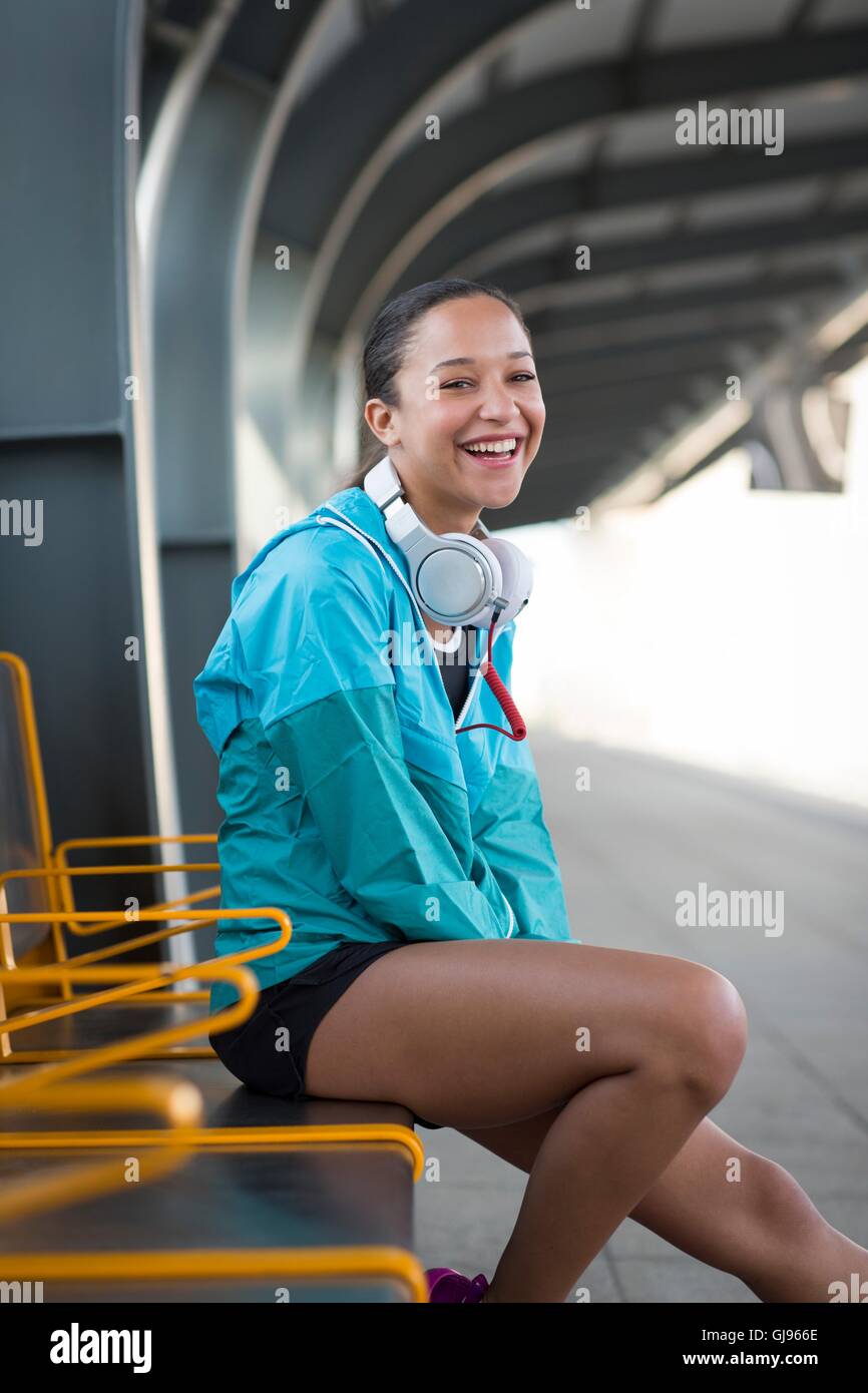 MODEL RELEASED. Young woman sitting on railway platform smiling. Stock Photo