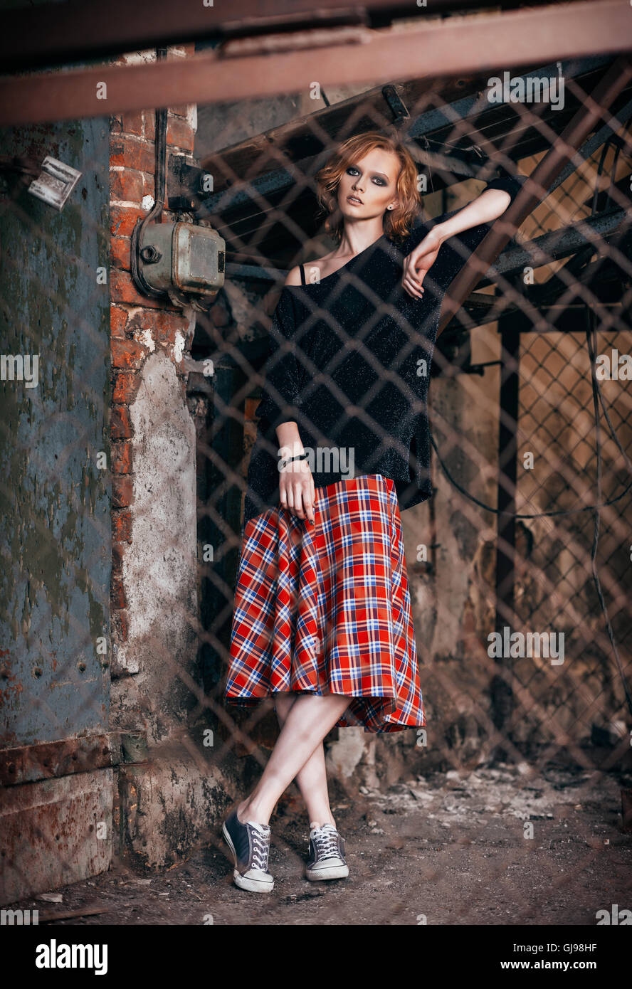 Portrait of a beautiful grunge girl in plaid skirt and sweater standing behind metallic lattice Stock Photo