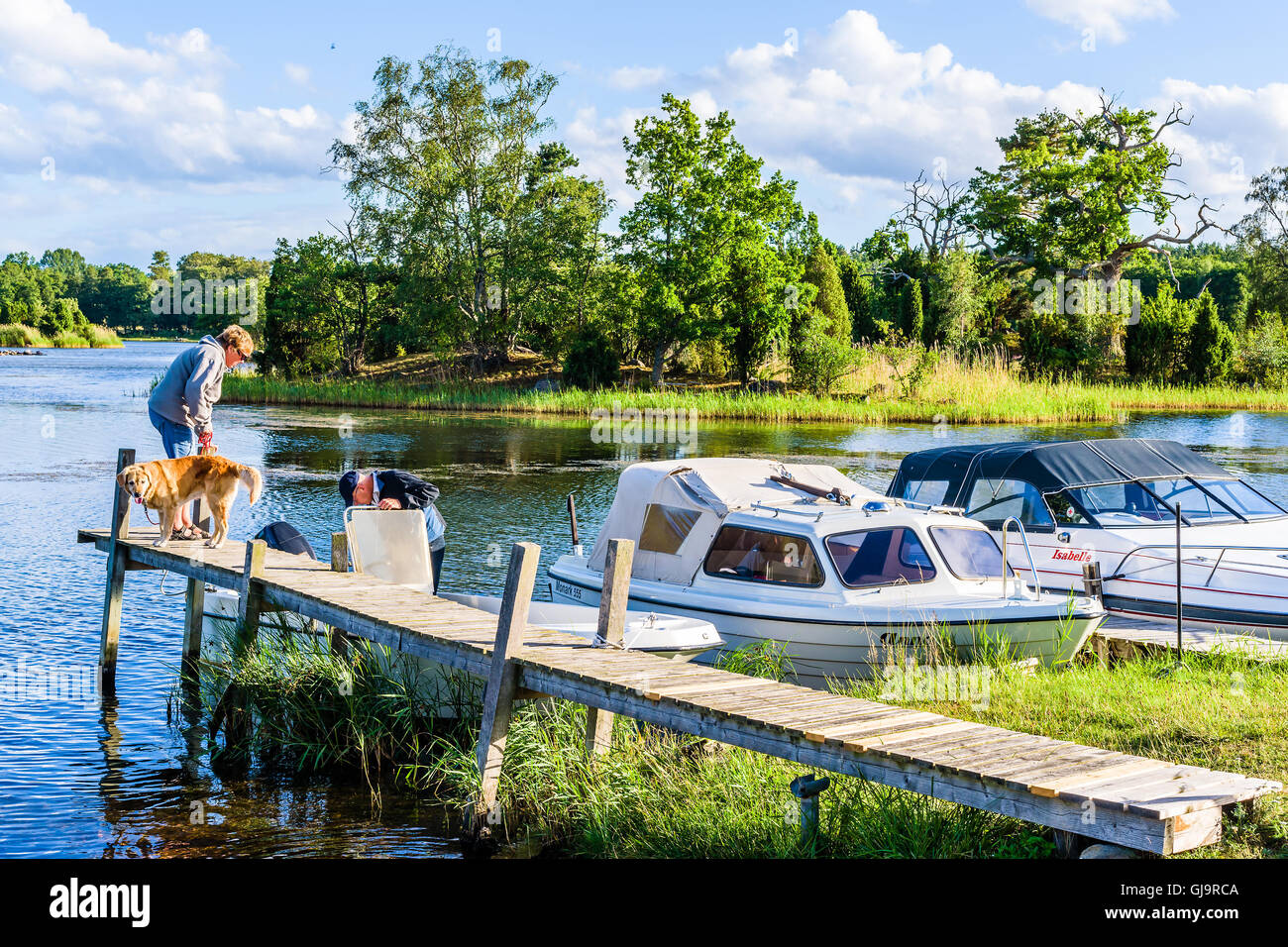 Pataholm, Sweden - August 9, 2016: Senior couple getting ready to go for a boat trip with their dog. Woman and dog on pier while Stock Photo
