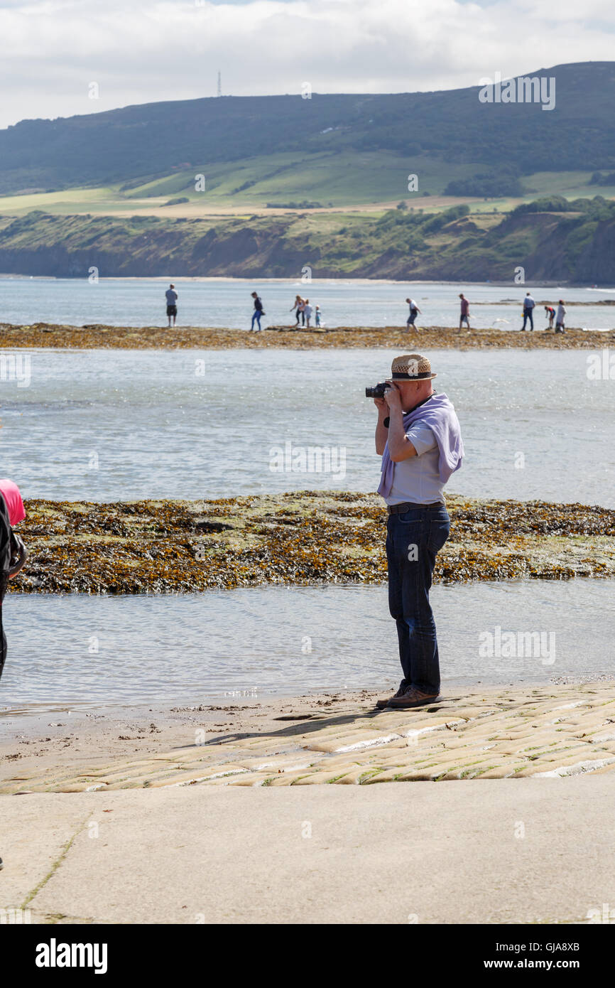 Man taking a photo with a camera. In Robin Hoods Bay, North Yorkshire, England. Stock Photo