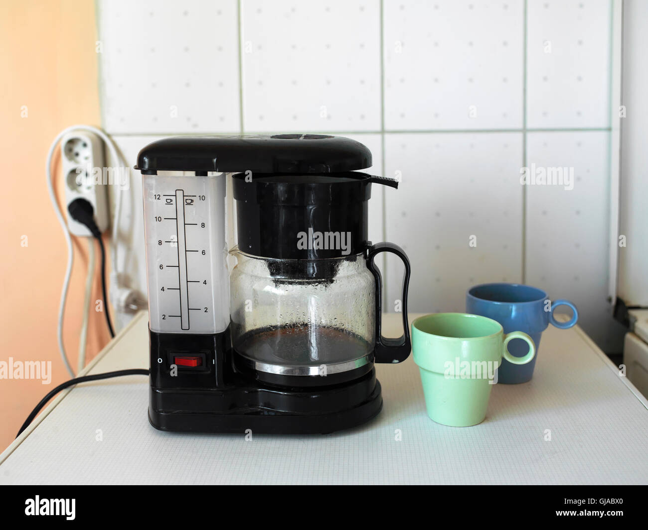 Two mugs next to electric coffee maker against the kitchen wall