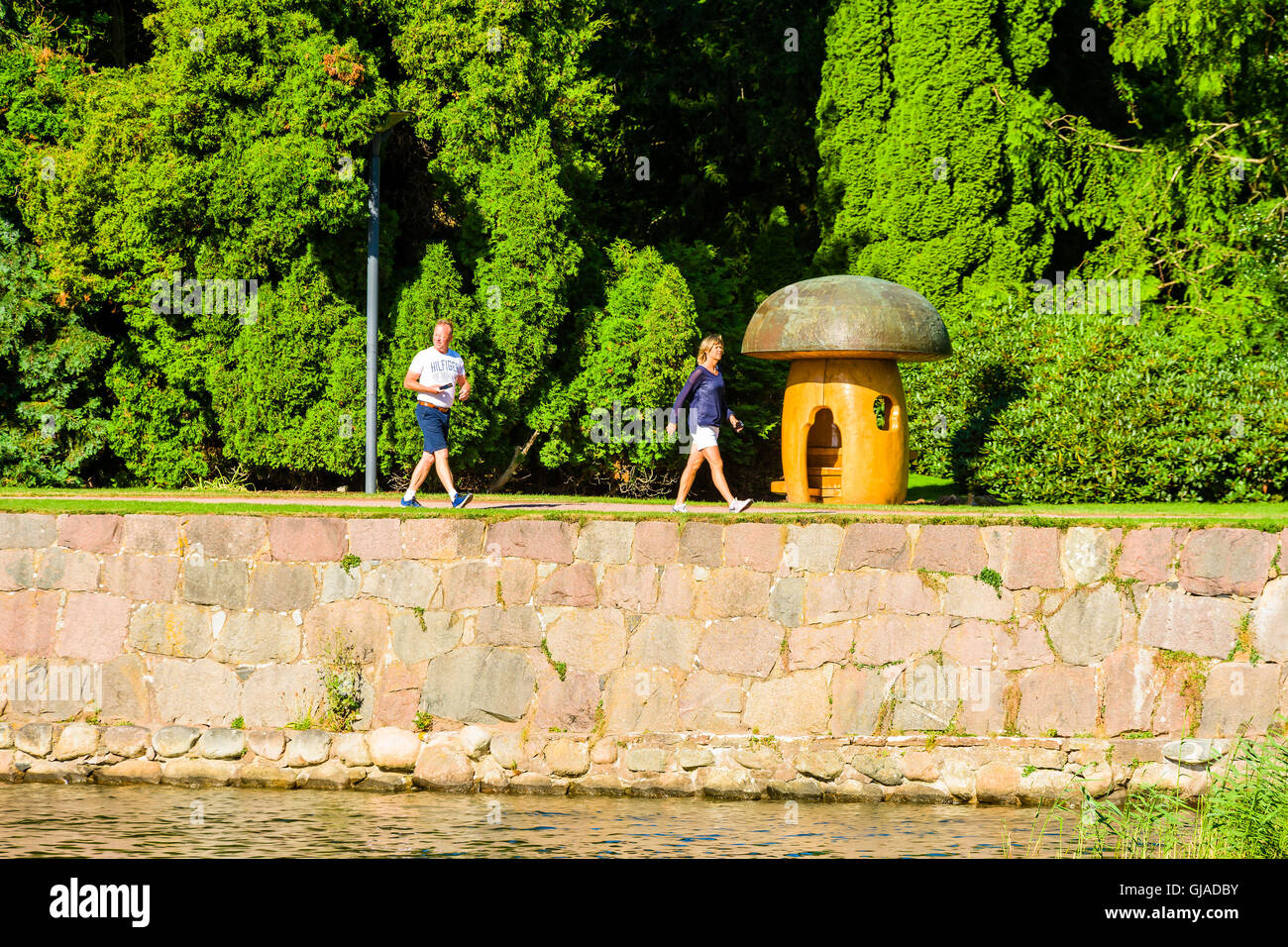 Kalmar, Sweden - August 10, 2016: Two persons walk by a large artificial mushroom in the public park Stadsparken in town. Stock Photo