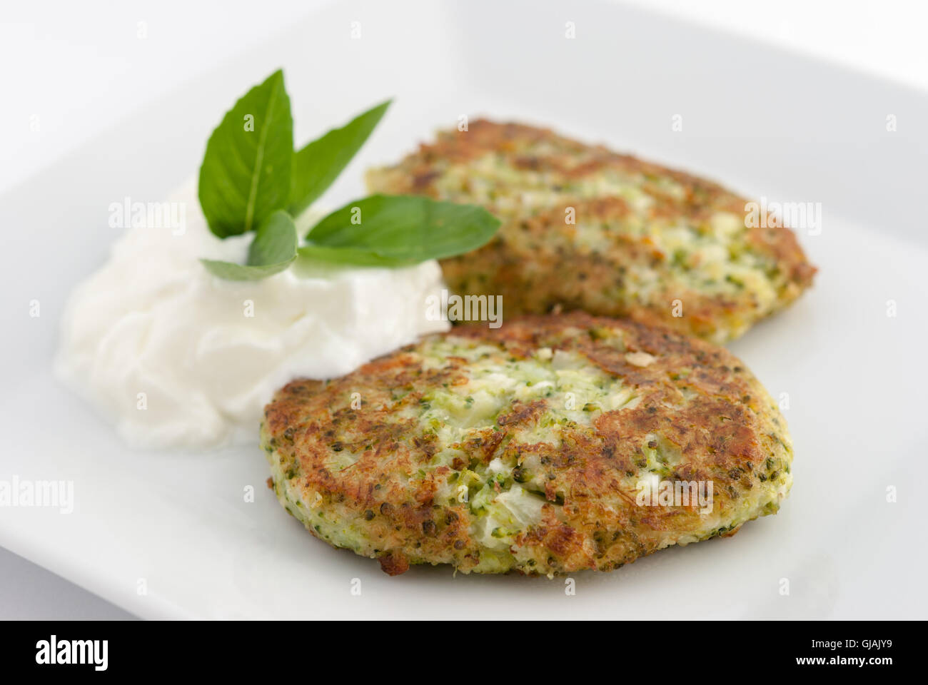 Broccoli and cheese pancakes served with traditional Greek yogurt on a white plate closeup. Stock Photo