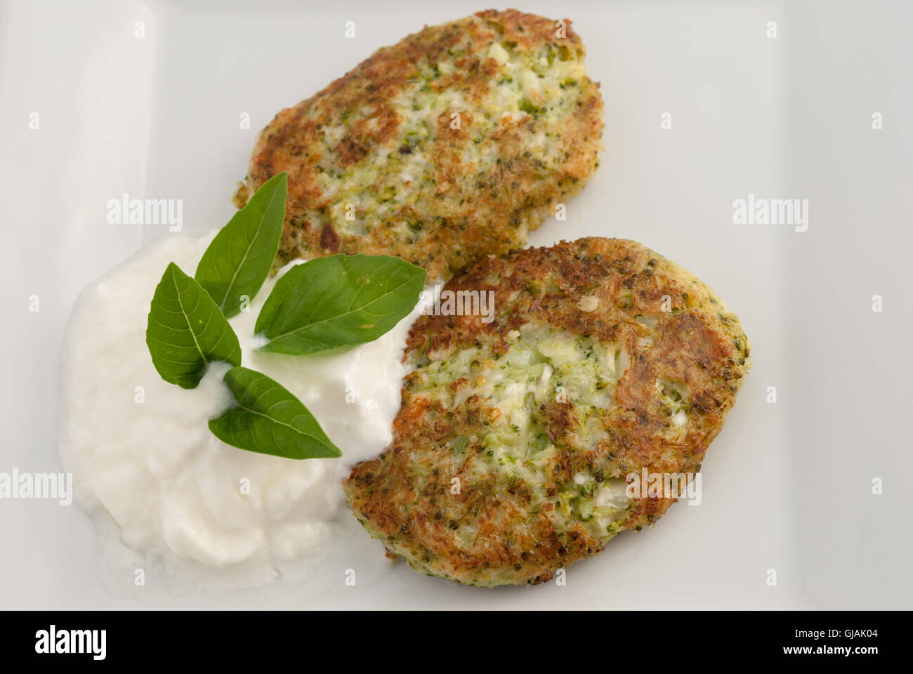 Broccoli and cheese pancakes served with traditional Greek yogurt on a white plate closeup. Stock Photo