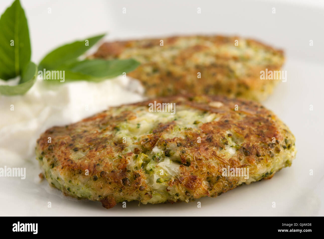 Broccoli and cheese pancakes served with traditional Greek yogurt on a white plate closeup. Stock Photo