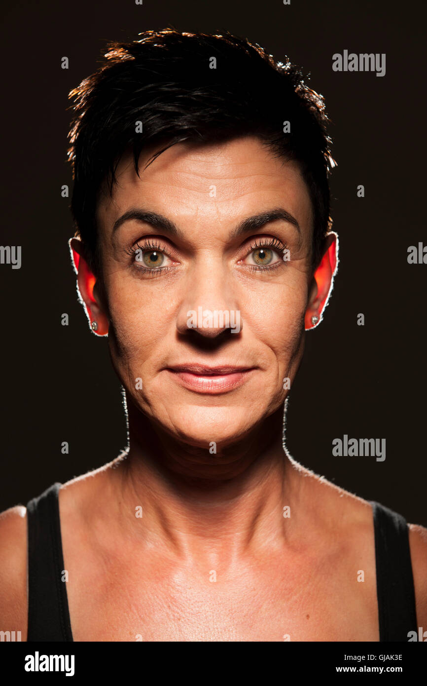 Head and shoulders portrait looking a middle-aged black-haired woman black background in the spot light in the camera. Stock Photo