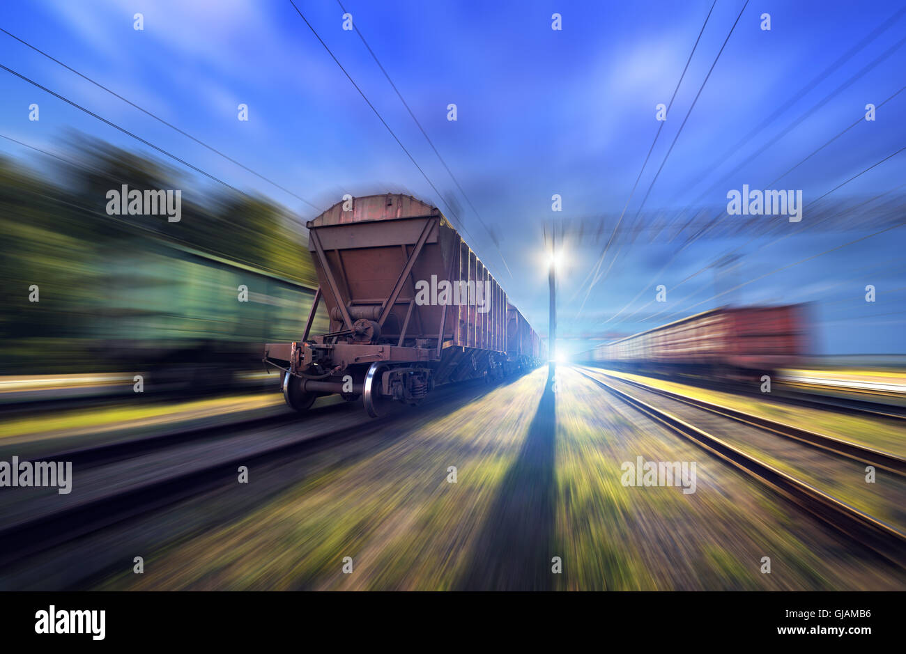Railway station with cargo wagons and train light in motion at night. Railroad with motion blur effect. Heavy industry Stock Photo