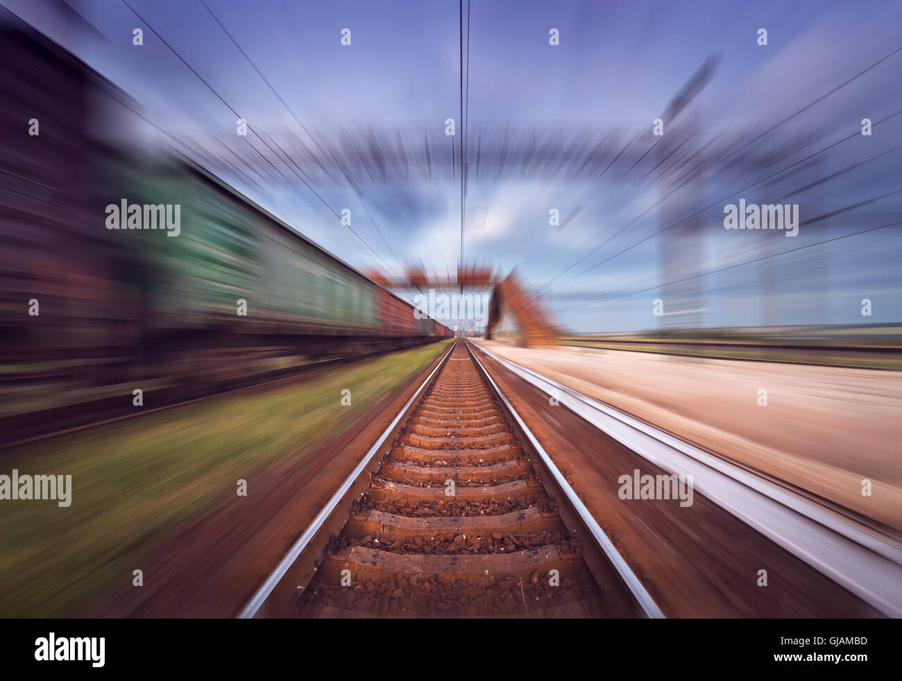 Railway station with cargo wagons in motion at sunset. Railroad with motion blur effect. Railway platform at dusk. Stock Photo
