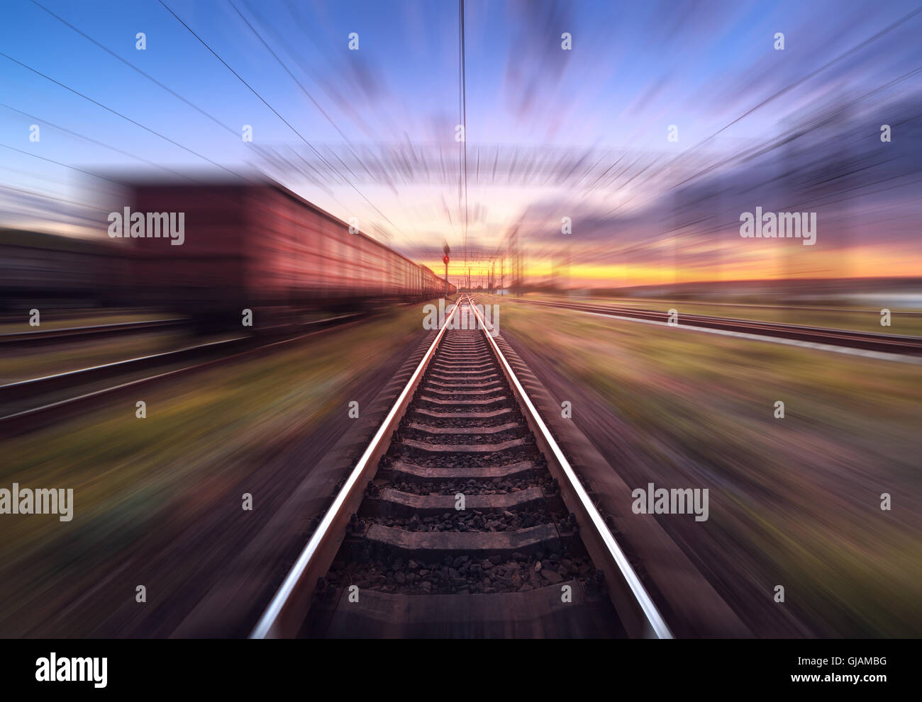 Railway station with cargo wagons in motion at sunset. Railroad with motion blur effect. Railway platform at dusk. Stock Photo