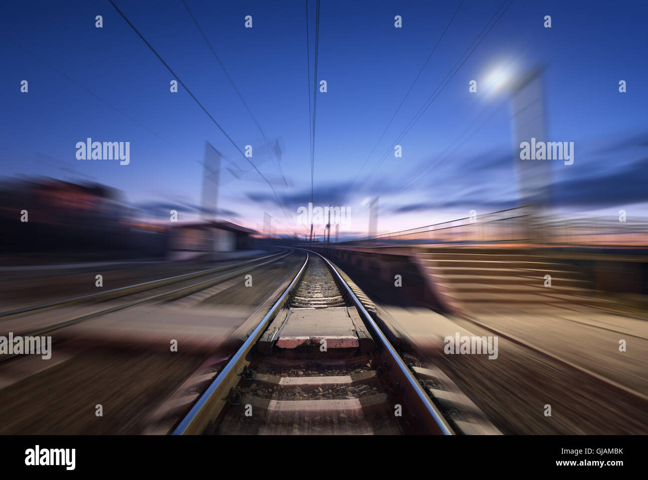 Railway platform with motion blur effect on the background of blue sky at night. Railway station. Railroad Stock Photo