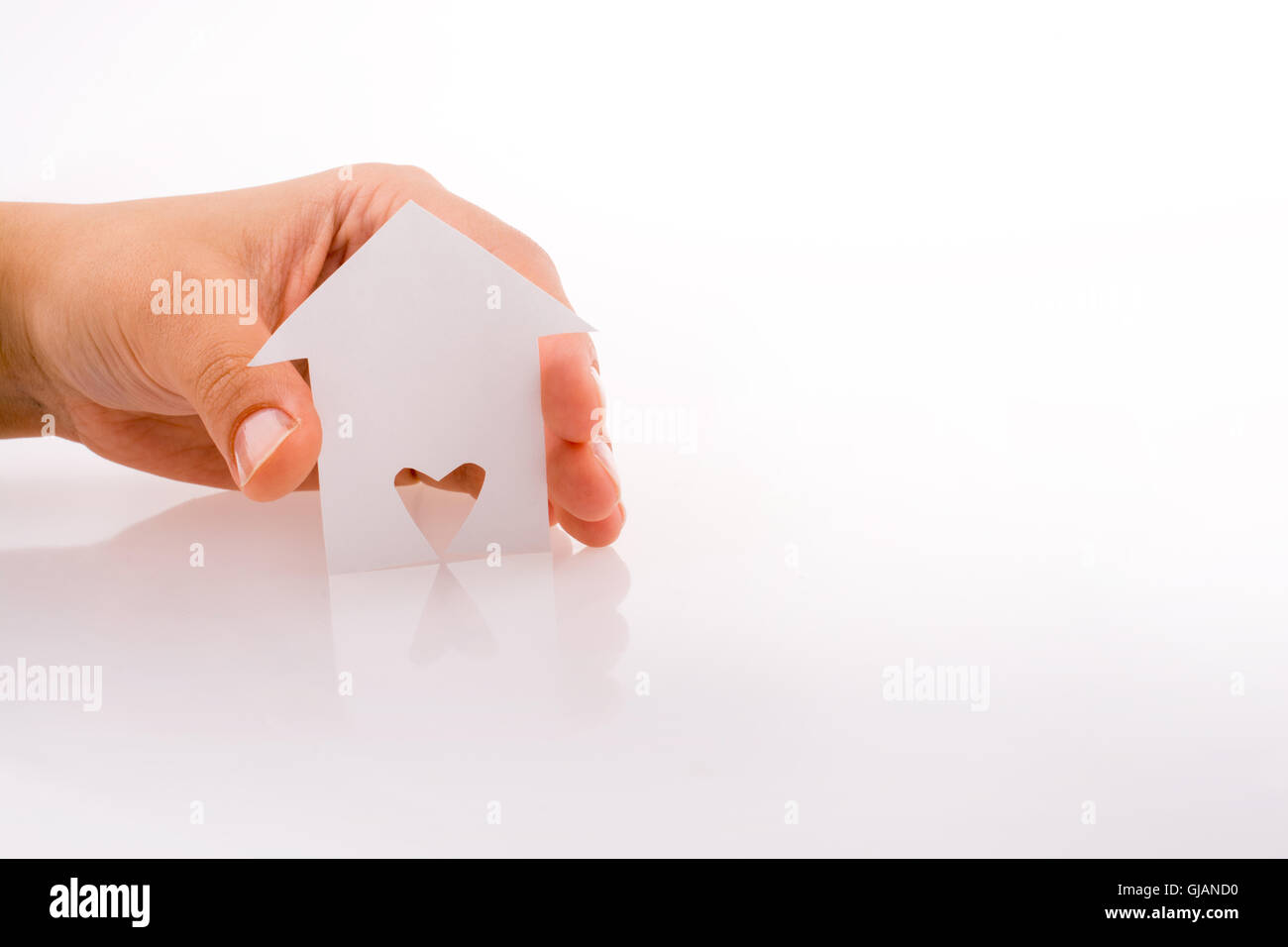 Hand holding a paper house with a heart carved in it on a white ...
