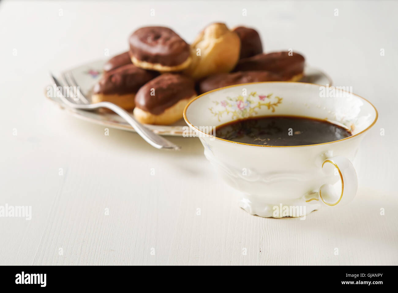 French Chocolate cake, eclairs with a cup of hot black coffee in a vintage crockery, dessert fork. White wooden background Stock Photo
