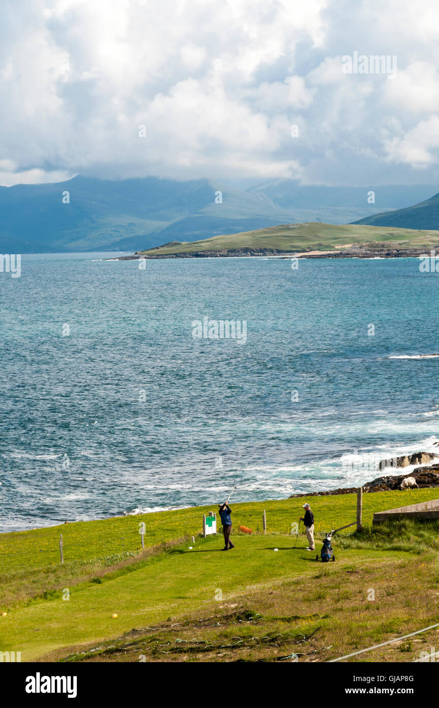 Two golfers teeing off at Isle Of Harris Golf Course in the Outer Hebrides with Sound of Taransay and North Harris in background Stock Photo