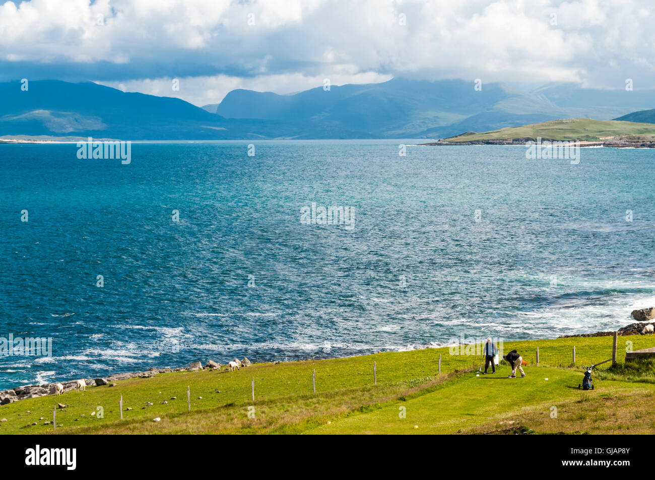 Two golfers teeing off at Isle Of Harris Golf Course in the Outer Hebrides with Sound of Taransay and North Harris in background Stock Photo