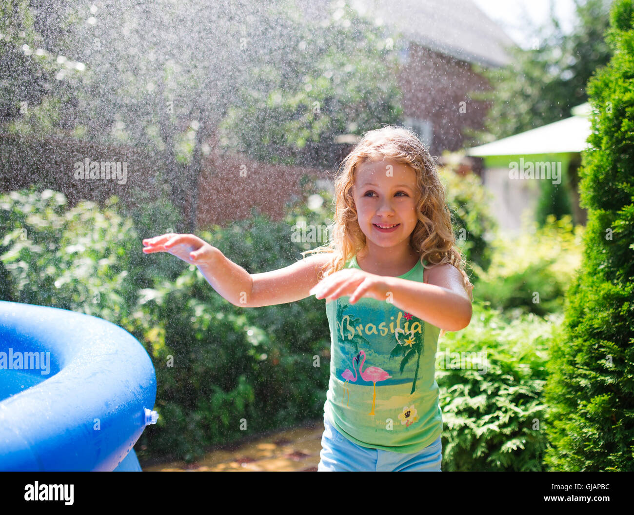 Preschooler cute girl playing with garden sprinkler. Summer outdoor water fun in the backyard. Stock Photo