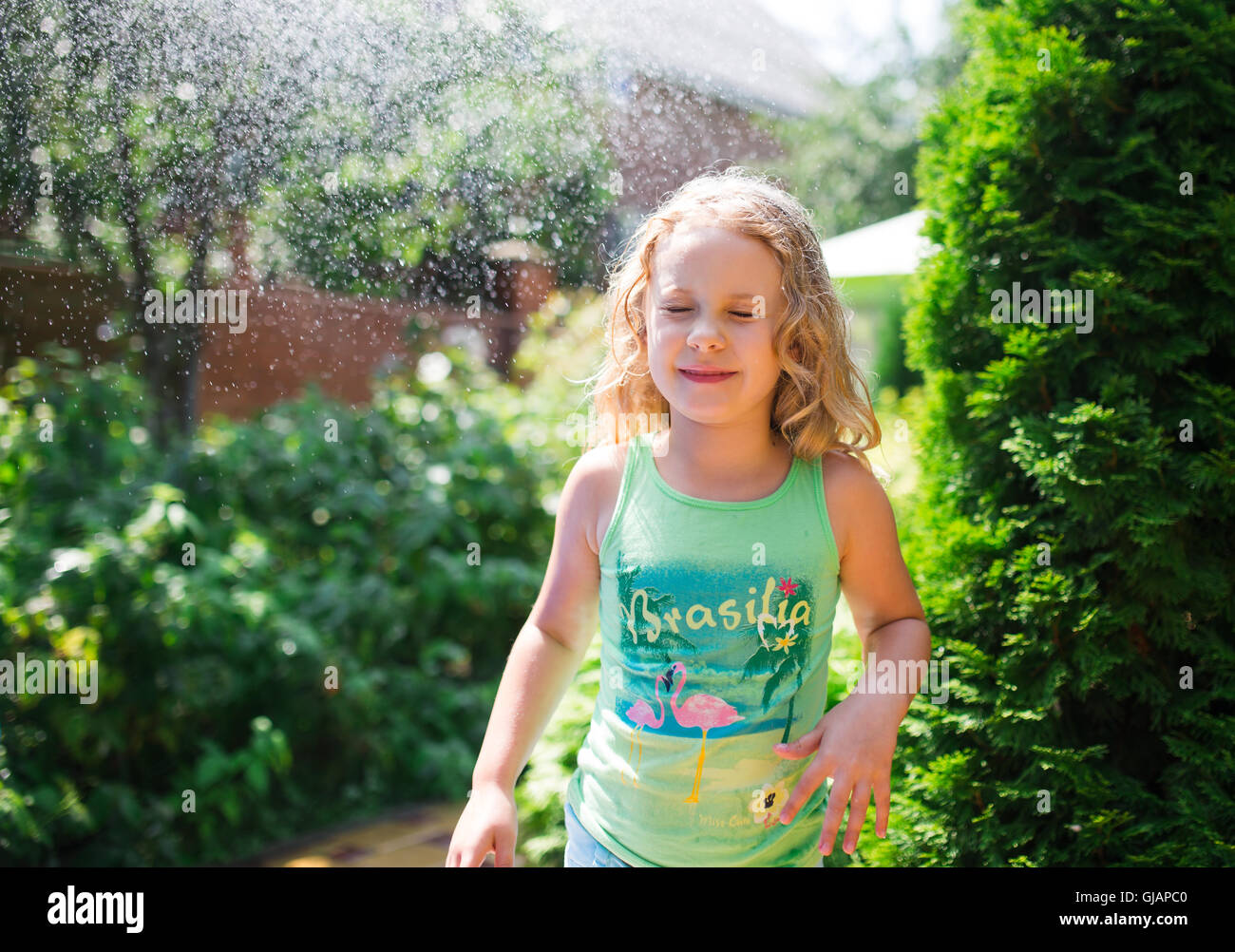 Preschooler cute girl playing with garden sprinkler. Summer outdoor water fun in the backyard. Stock Photo