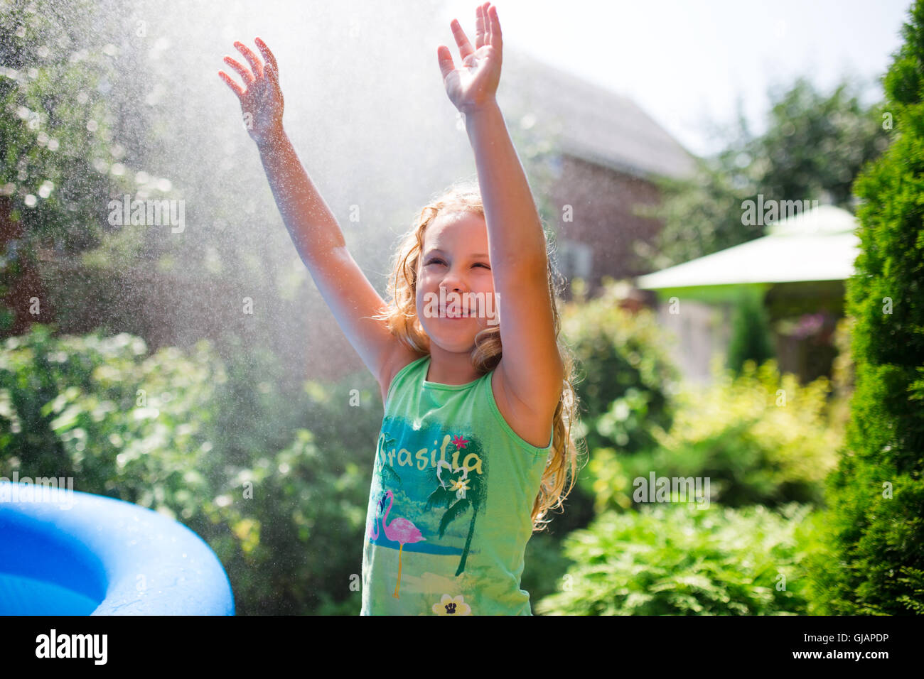 Preschooler cute girl playing with garden sprinkler. Summer outdoor water fun in the backyard. Stock Photo