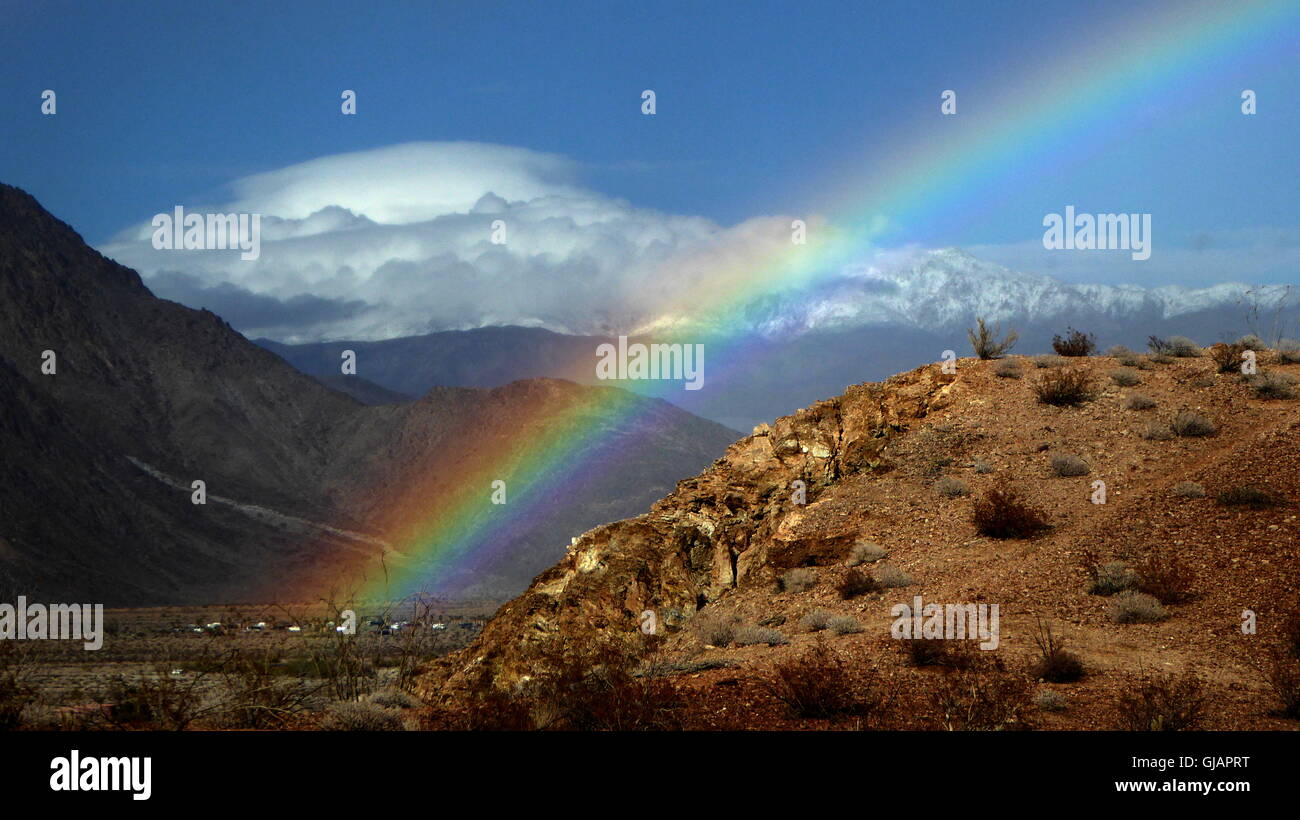 Rainbow comes out of the mountain with clear skies and distant white clouds Stock Photo